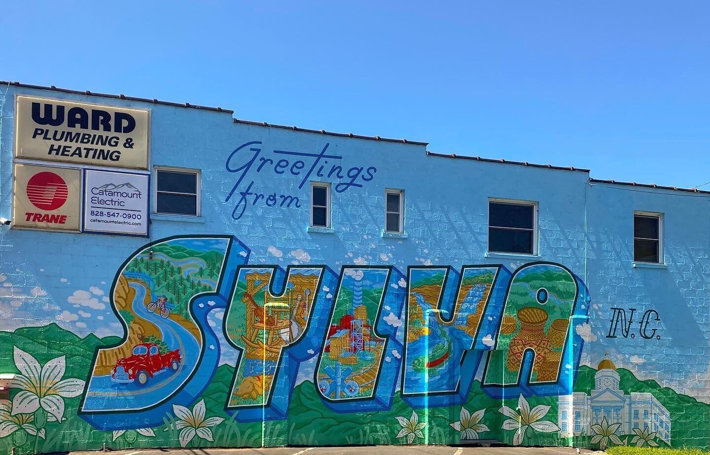 Un bâtiment orné d’une fresque murale représentant un grand panneau avec l’inscription « SYUWA » et un autre panneau indiquant « Salutations de… ».