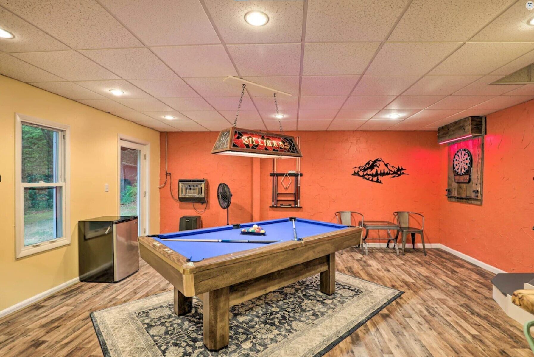 A pool table in a room with orange walls, a dartboard, and a billiards sign.