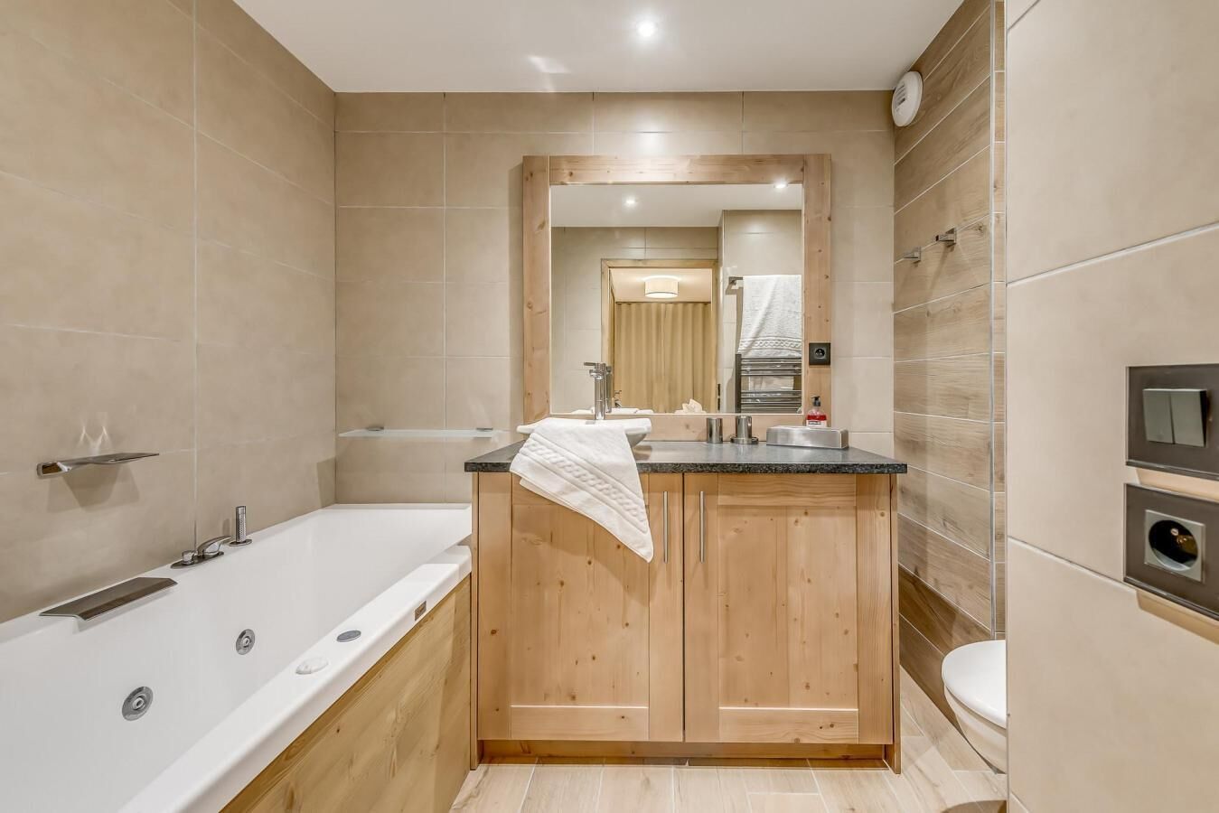 A modern bathroom with a wooden vanity, a large bathtub, and a toilet.