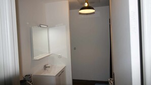 En smal gang med en hvid vask og et spejl, en hængende pendel samt en dør til højre.