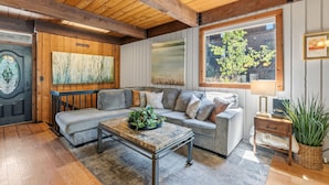A cozy living room with a grey sofa, a coffee table, and a large window with a view of greenery. - Cozy Breckenridge Condo Near Peak 9 & Main Street (Breckenridge)