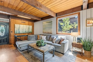 A cozy living room with a grey sofa, a coffee table, and a large window with a view of greenery. - Cozy Breckenridge Condo Near Peak 9 & Main Street (Breckenridge)