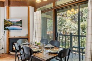 A dining area with a table set for four, a fireplace, and a large window with a view of trees.