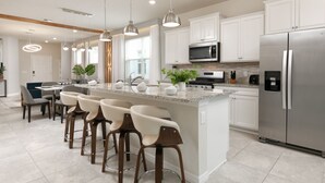 A modern kitchen with white cabinets, stainless steel appliances, and a central island with bar stools. - Capture Every Moment: Insta-Worthy 5BD, Theme Bd, Pv Pool, Avengers Game Room! (Davenport)