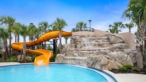 A pool with a yellow water slide, palm trees, and a rocky waterfall backdrop. - Capture Every Moment: Insta-Worthy 5BD, Theme Bd, Pv Pool, Avengers Game Room! (Davenport)