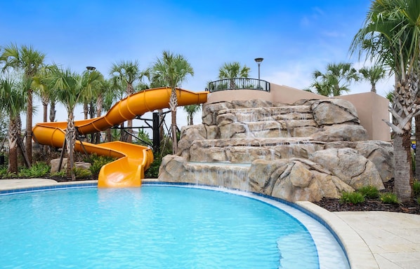 A pool with a yellow water slide and a rock waterfall.