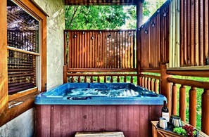 Een hottub met een houten terras en een houten omheining, omgeven door groen.