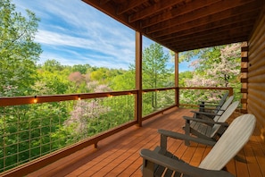 A wooden deck with outdoor seating and a view of a forested area.