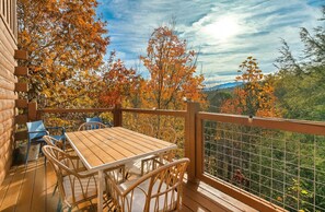 Een houten terras met tafel en stoelen, met uitzicht op een bos in herfstkleuren.