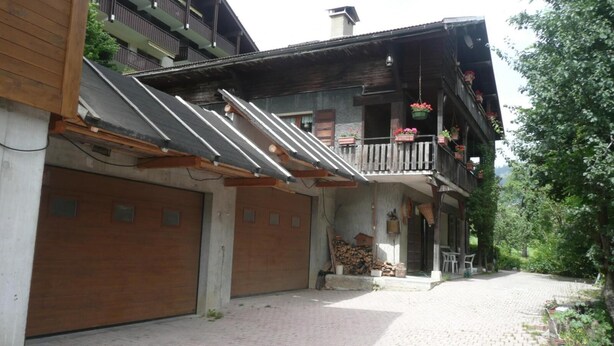 Ein Gebäude mit Holzfassade, einem Balkon mit hängenden Blumenkörben und einem gepflasterten Auffahrt.