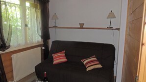 Ein gemütliches Zimmer mit einer schwarzen Couch, zwei Kissen, einem kleinen Tisch mit einer Weinflasche und Gläsern sowie zwei Lampen auf Regalen.