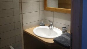 A bathroom with a wooden ceiling, a white sink with a mirror above it, and a towel rack.
