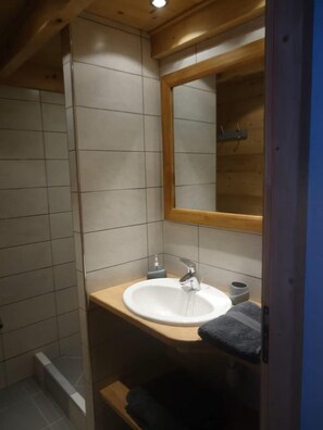 A bathroom with a wooden ceiling, a white sink with a mirror above it, and a towel rack.