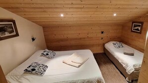 A small, cozy room with wooden walls and ceiling, two beds with white bedding, and a small table with a lamp.
