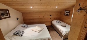 A small, cozy room with wooden walls and ceiling, two beds with white bedding, and a small table with a lamp.