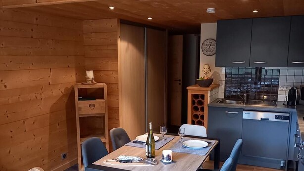 A cozy wooden interior with a dining area, kitchen, and a bed.