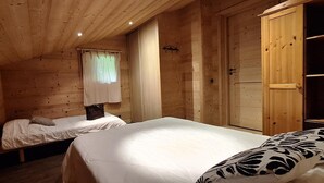 A wooden cabin room with two beds, a window with curtains, and a wooden wardrobe.