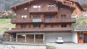 A multi-story wooden building with balconies, a ski resort sign, and a parking area.
