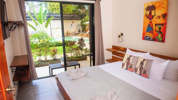 A hotel room with a bed, a view of a pool, and a painting on the wall. - VillasLunaAfricana–101 (Puerto Viejo de Talamanca)