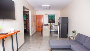 A modern living room with a grey sofa, a small table, and a kitchen area in the background. - VillasLunaAfricana–101 (Puerto Viejo de Talamanca)