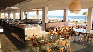 A modern restaurant with a glass dining area, a bar, and seating with ocean views.