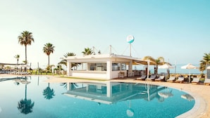 A swimming pool with lounge chairs and umbrellas, a small building with a satellite dish, and palm trees.