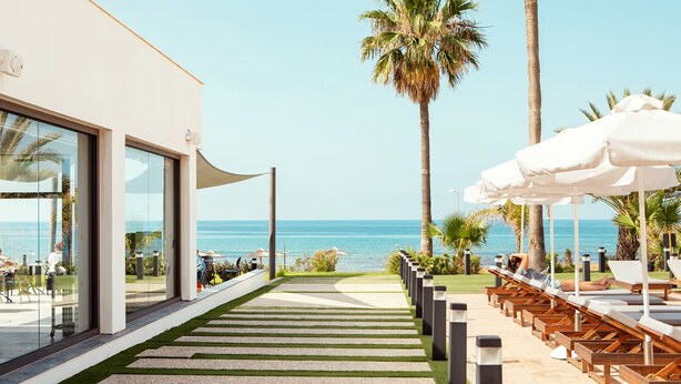 A pathway leading to a beachside lounge area with sun loungers and umbrellas, overlooking the ocean.