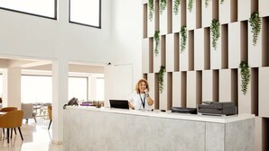 A modern reception desk with a white countertop, a phone, and a laptop. There are vertical panels with greenery on the wall behind the desk.