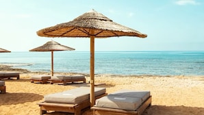 A beach with wooden lounge chairs and thatched umbrellas.