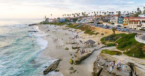 A coastal beach with rocky outcrops, a promenade, and buildings in the background. - Gorgeous 4-bd Haven, steps from Windansea Beach (San Diego)