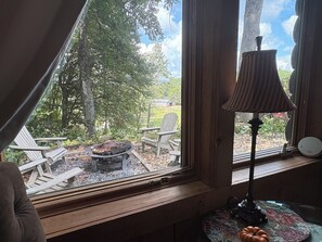Une pièce avec une fenêtre donnant sur un jardin, un banc en bois, une table avec une lampe et une petite citrouille.