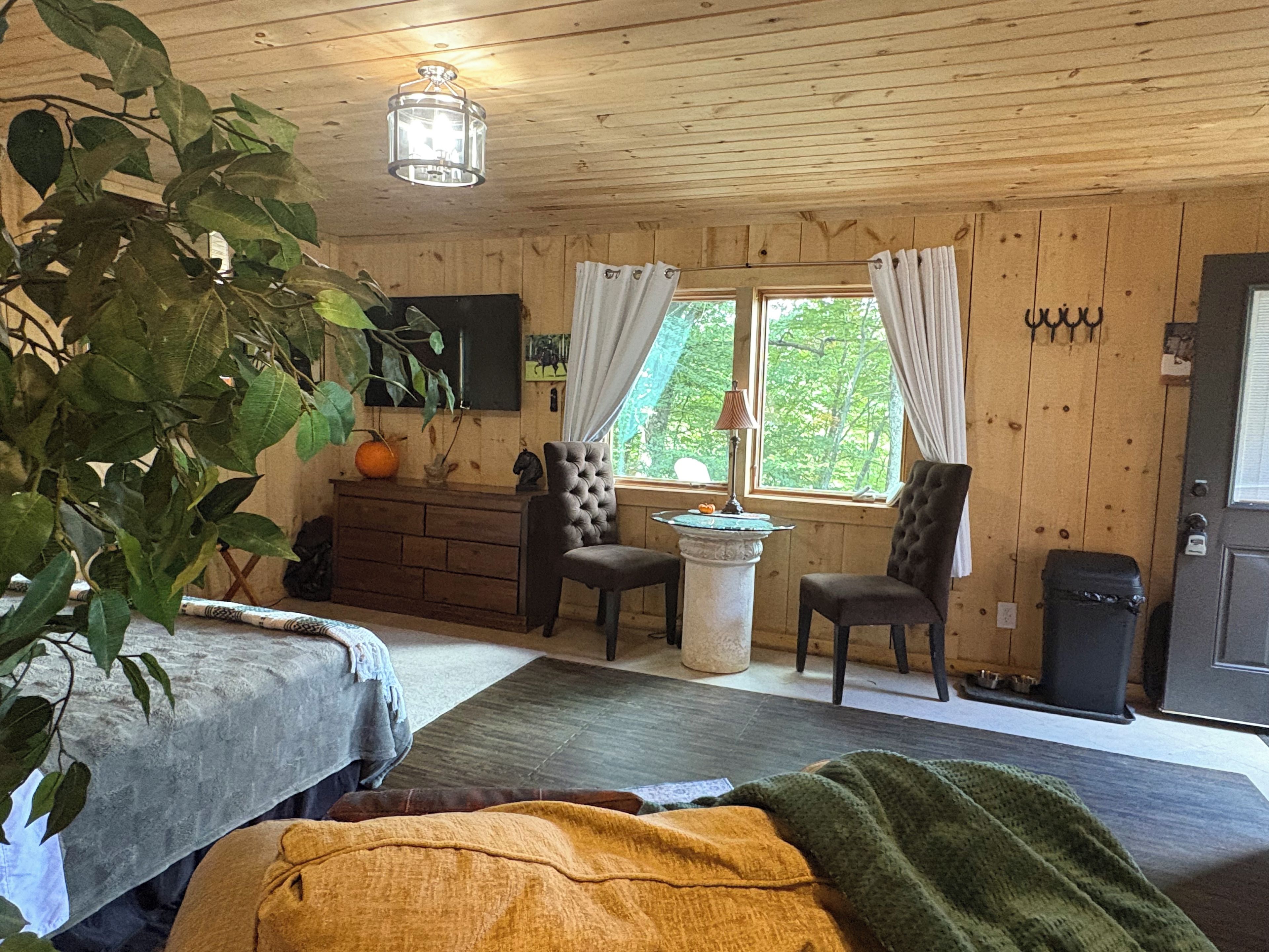 A cozy room with wooden walls, a bed, a dresser, two chairs, a table, and a window with curtains.