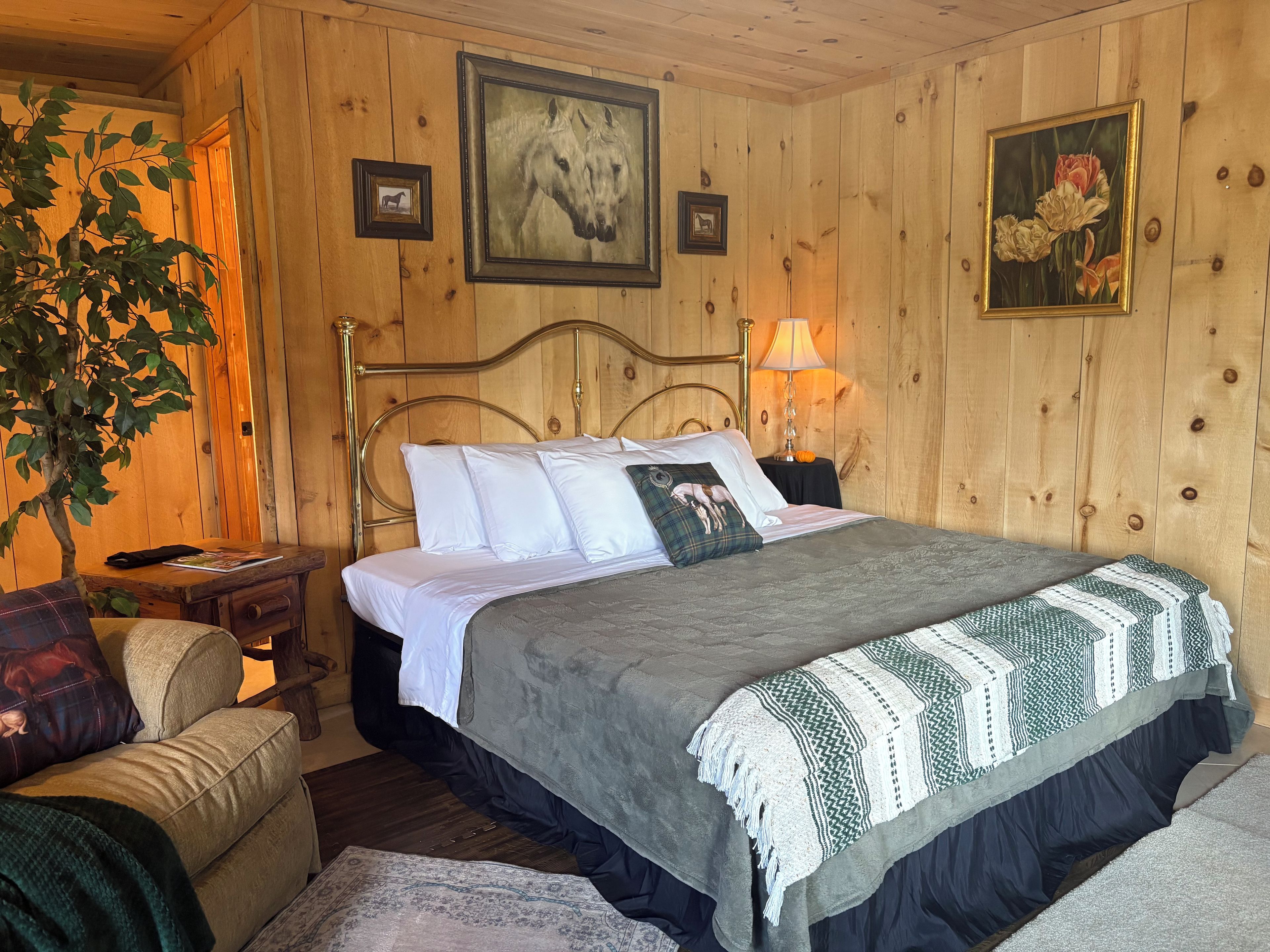A wooden-paneled room with a bed, a chair, a lamp, and framed pictures on the wall.