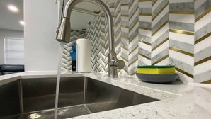 Et køkken med en stålvask, en moderne hane og et backsplash med et fiskebensmønster.