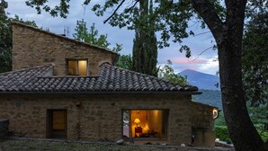 A stone house with a tiled roof, a visible interior with a lamp, and a mountainous backdrop. - Pool, Villa La Colline, beautiful view of Mt Ventoux (Suzette)