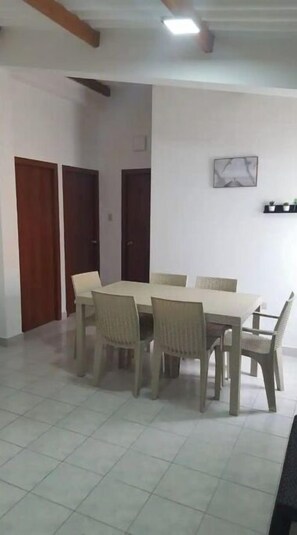 Un coin repas avec une table rectangulaire entourée de chaises, un ventilateur de plafond et un tableau encadré au mur.