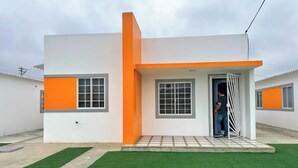 Une maison moderne à deux étages, dotée d’un toit plat, d’un petit porche et d’une pelouse verdoyante.