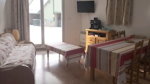 A room with a bed, a table, a TV, and a window with curtains.
