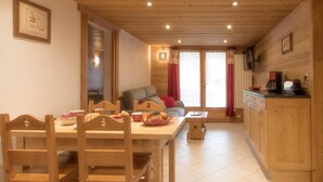 A wooden dining table with chairs, a kitchen area with cabinets, and a sofa in a room with wooden walls and ceiling. - 20m from ski slopes, 1st floor, balcony, parking, tv, 52m², Le Grand Bornand (Le Grand-Bornand)