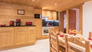 A wooden cabin-style kitchen with a dining area, featuring wooden cabinets, a microwave, a stove, and a dining table with chairs. - 20m from ski slopes, 1st floor, balcony, parking, tv, 52m², Le Grand Bornand (Le Grand-Bornand)