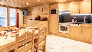 A wooden interior with a dining table, chairs, a kitchen with wooden cabinets, a microwave, and a television. - 20m from ski slopes, 1st floor, balcony, parking, tv, 52m², Le Grand Bornand (Le Grand-Bornand)