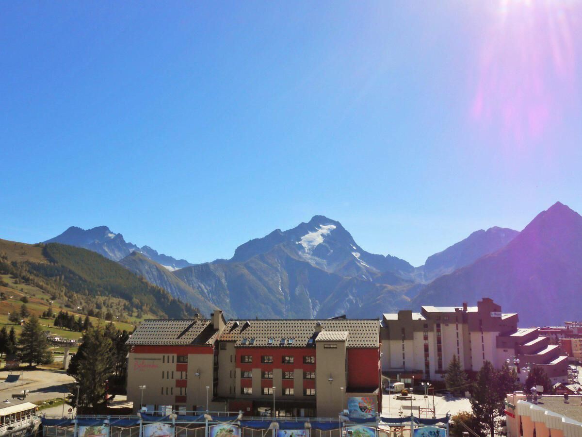 Ein Hotel mit Blick auf die Berge, mit einer roten und beigen Fassade, mehreren Stockwerken und einem Parkplatz im Vordergrund.
