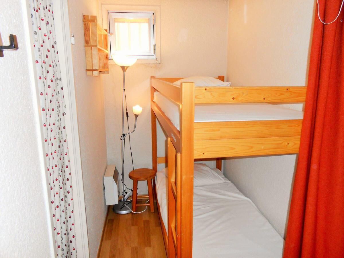 Une petite pièce, de taille modeste, avec un lit superposé, une table de chevet avec une lampe et une fenêtre avec un rideau.