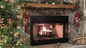 A fireplace with a stone wall backdrop, a Christmas tree with ornaments, and stockings on the mantel. - Rose Creek Retreat (Franklin)