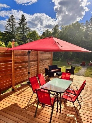 Eine Terrasse im Freien mit Tisch, Stühlen, einem roten Sonnenschirm und einem Holzzaun.