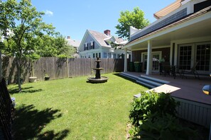 Ein Garten mit einer Holzterrasse, einem Brunnen und einem Haus im Hintergrund.