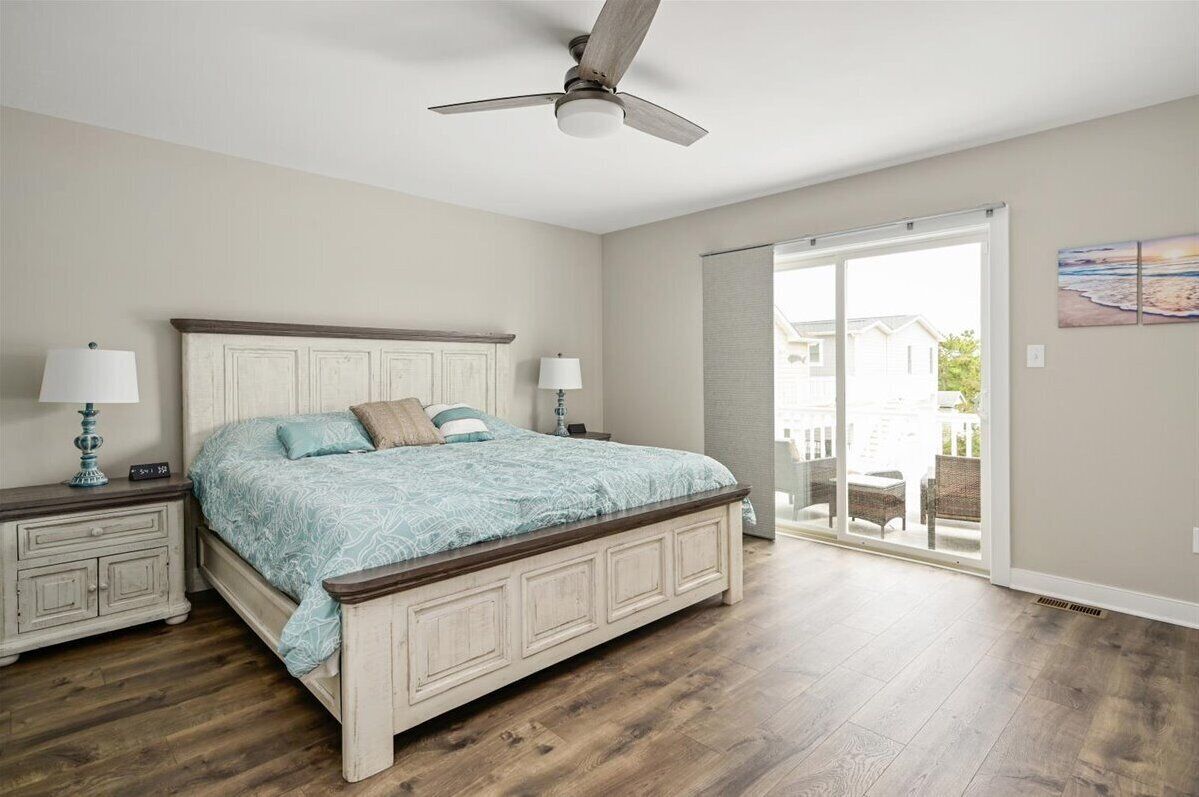 A bedroom with a bed, nightstands, a ceiling fan, and a sliding glass door leading to a balcony.
