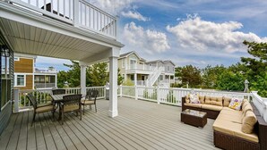 Eine Holzterrasse mit Gartenmöbeln, darunter eine Sitzecke mit Sofa und Sesseln, sowie ein überdachter Bereich mit Geländer.