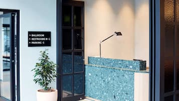Un área de recepción con una planta en maceta, un mostrador y un cartel que indica el camino al salón de baile, los baños y el estacionamiento.
