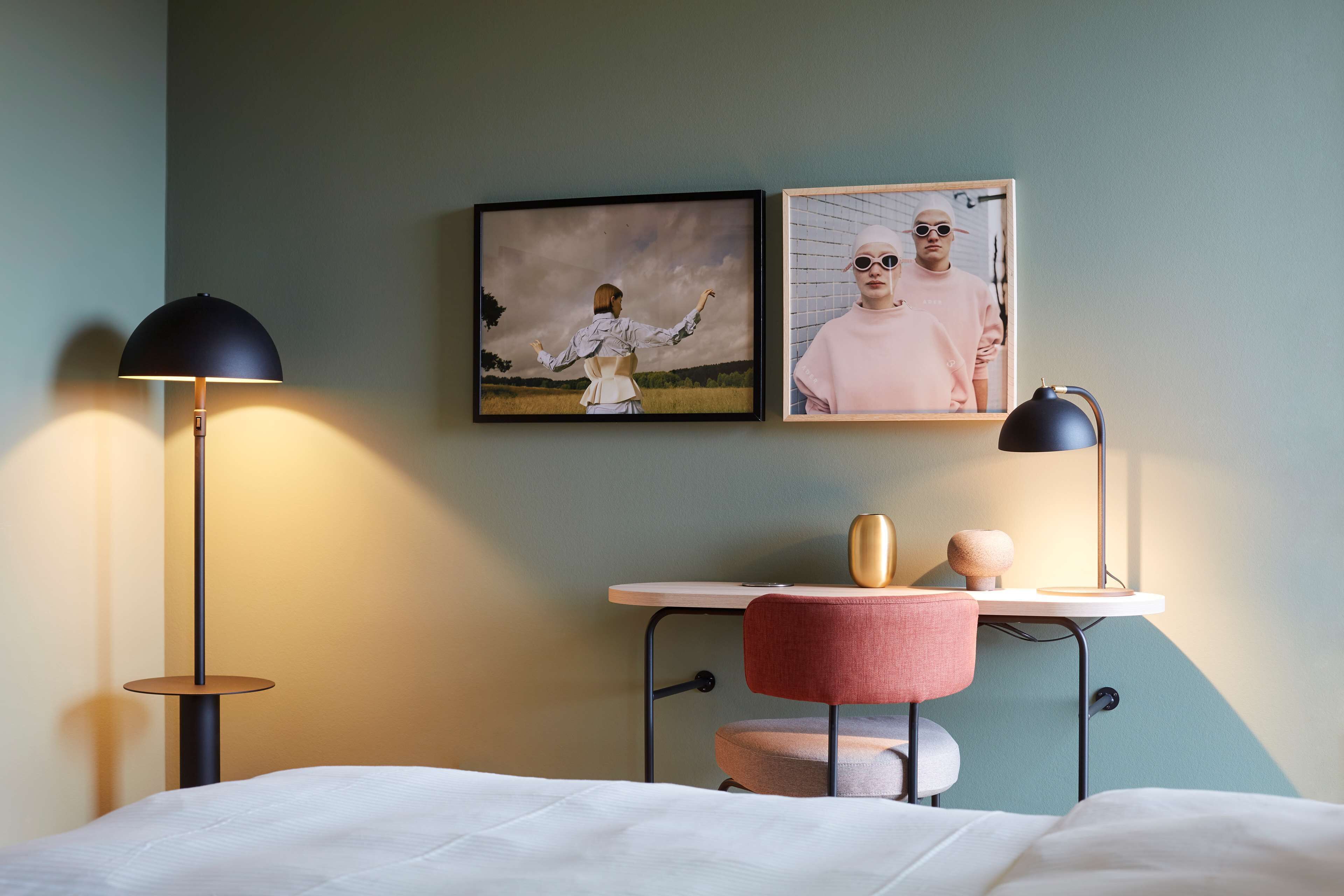 A neatly arranged hotel room with a bed, a desk with a chair, a lamp, and two framed pictures on the wall.